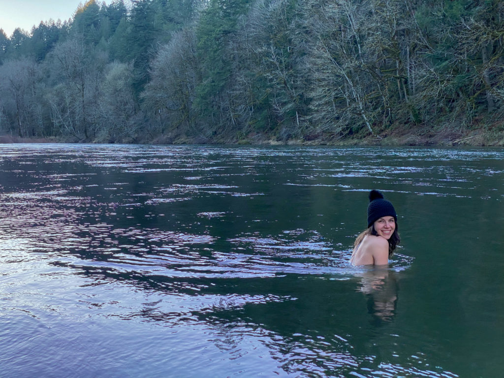 Woman is up to her shoulders in the river near sunset smiling at the camera