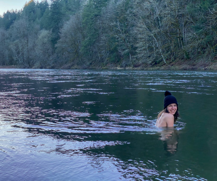 Woman is up to her shoulders in the river near sunset smiling at the camera